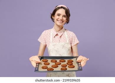 Young Smiling Happy Housewife Housekeeper Chef Cook Baker Woman Wearing Pink Apron Show Chocolate Cookies Biscuits On Baking Sheet Isolated On Pastel Violet Background Studio. Cooking Food Concept.