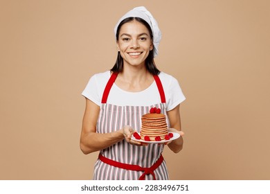 Young smiling happy housewife housekeeper chef baker latin woman wear striped apron toque hat hold pancakes on plate with raspberries isolated on plain pastel light beige background. Cook food concept - Powered by Shutterstock