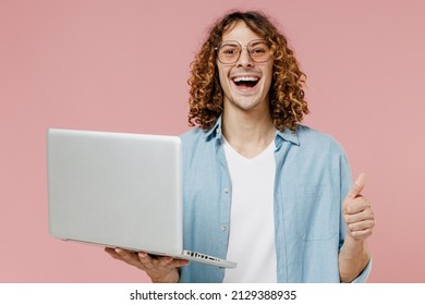 Young Smiling Happy Man 20s With Long Curly Hair In Blue Shirt White T-shirt Glasses Hold Use Work On Laptop Pc Computer Show Thumb Up Isolated On Pastel Plain Pink Color Background Studio Portrait