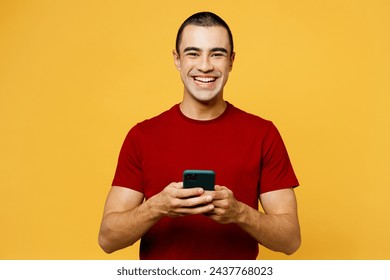 Young smiling happy middle eastern man he wear red t-shirt casual clothes hold in hand use mobile cell phone look camera isolated on plain yellow orange background studio portrait. Lifestyle concept - Powered by Shutterstock