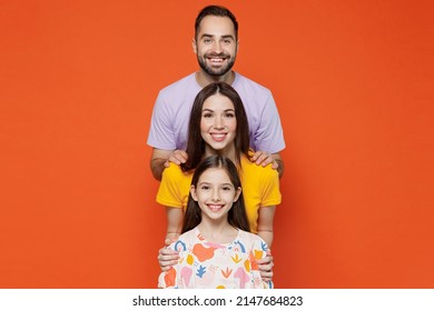 Young Smiling Happy Parents Mom Dad With Child Kid Daughter Teen Girl In Basic T-shirts Stand Behind Each Other Isolated On Yellow Background Studio Portrait. Family Day Parenthood Childhood Concept.