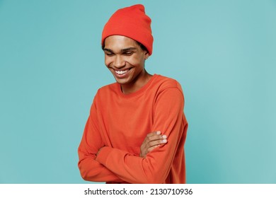 Young Smiling Happy Positive African American Man 20s In Orange Shirt Hat Hold Hands Crossed Folded Laughing Isolated On Plain Pastel Light Blue Background Studio Portrait. People Lifestyle Concept