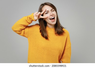 Young smiling happy positive satisfied cheerful attractive woman 20s wearing casual knitted yellow sweater covering eye with victory v-sign gesture isolated on grey color background studio portrait.
