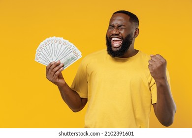 Young smiling happy rich black man 20s wearing bright casual t-shirt holding fan of cash money in dollar banknotes do winner gesture isolated on plain yellow color background. People lifestyle concept - Shutterstock ID 2102391601