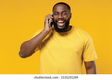 Young Smiling Happy Satisfied Black Man 20s In Bright Casual T-shirt Speaking Talking On Mobile Cell Phone Chatting Isolated On Plain Yellow Color Background Studio Portrait. People Lifestyle Concept