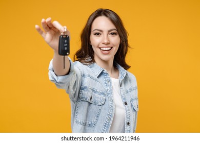 Young smiling happy satisfied excited successful brunette woman 20s in denim shirt white t-shirt hold in hands giving car keys show thumb up like gesture isolated on yellow background studio portrait