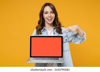 Young Smiling Happy Satisfied Fun Woman 20s In Denim Shirt White T-shirt Point Index Finger On Laptop Pc Computer With Blank Screen Workspace Area Chat Isolated On Yellow Background Studio Portrait.