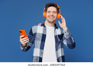 Young smiling happy satisfied man wear shirt white t-shirt casual clothes listen to music in headphones use mobile cell phone isolated on plain blue cyan background studio portrait. Lifestyle concept - Powered by Shutterstock