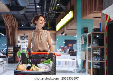 Young smiling happy satisfied woman 20s wear casual clothes shopping at supermaket store with grocery cart look aside produce inside hypermarket. People lifestyle purchasing gastronomy food concept