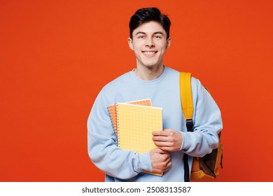 Young smiling happy smart fun cool man student he wearing blue casual clothes backpack bag holding books looking camera isolated on plain red orange background. High school university college concept - Powered by Shutterstock