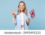 Young smiling happy student woman she wears white top shirt casual clothes hold in hand British flag look camera isolated on plain pastel light blue cyan background studio portrait. Lifestyle concept