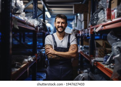 Young smiling happy tattooed bearded worker in overalls standing in storage of import and export firm with arms crossed. - Powered by Shutterstock