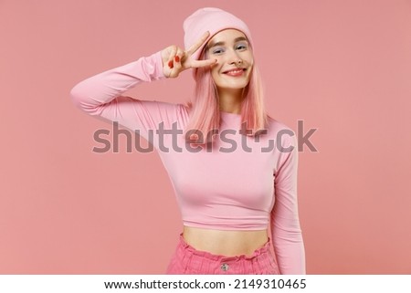 Young smiling happy woman 20s with bright dyed rose hair in rosy top shirt hat cover eye victory sign isolated on plain light pastel pink background studio portrait. People lifestyle fashion concept.