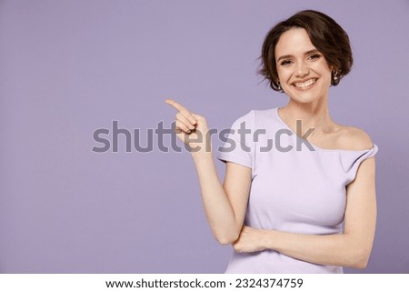 Young smiling happy woman 20s with bob haircut wearing white t-shirt point index finger aside on workspace area mock up isolated on pastel purple background studio portrait People lifestyle concept.