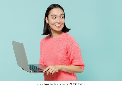 Young smiling happy woman of Asian ethnicity 20s in pink sweater hold use work on laptop pc computer look aside on workspace area isolated on pastel plain light blue color background studio portrait. - Shutterstock ID 2127045281