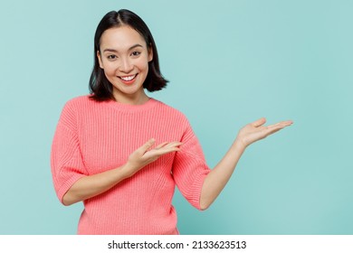 Young Smiling Happy Woman Of Asian Ethnicity 20s Wearing Pink Sweater Hands Arms Finger Aside On Workspace Area Mock Up Isolated On Pastel Plain Light Blue Background Studio. People Lifestyle Concept