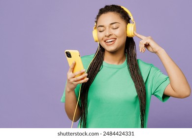 Young smiling happy woman with dreadlocks she wear green t-shirt casual clothes listen to music in headphones use mobile cell phone isolated on plain pastel light purple background. Lifestyle concept - Powered by Shutterstock