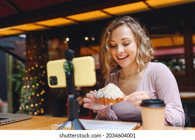 Young smiling happy woman wear casual clothes sit at table in cafe shop eat breakfast take picture on mobile cell phone do selfie shot photo of croissant drink coffee relaxing in restaurant indoors. - Shutterstock ID 2034604001