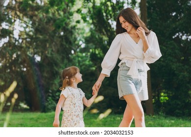 Young smiling happy woman in white clothes have fun with cute child baby girl 5-6 year old walk go along forest path hold arms Mommy rest with little kid daughter outdoor together Love family concept