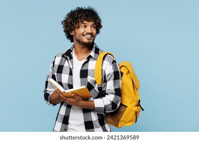 Young smiling Indian boy student he wears shirt casual clothes backpack bag read book hold notebook look aside isolated on plain pastel light blue background. High school university college concept - Powered by Shutterstock