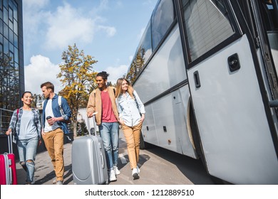 young smiling interracial couples with wheeled bags walking near travel bus at city street  - Powered by Shutterstock