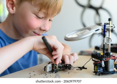 Young Smiling Inventor Kid Carefully Assembling Robotic Toy With Screwdriver, Working With Small Mechanical Parts, Using Magnifier Glass. STEM Education