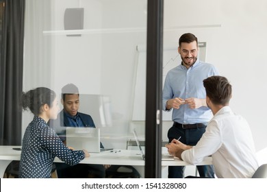 Young smiling male leader holds meeting, discussing work moments with multiracial colleagues or clients. Confident boss presenting plan of new start-up project to motivate employees in boardroom - Shutterstock ID 1541328080