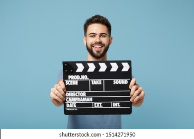 Young smiling man in casual clothes posing isolated on blue wall background, studio portrait. People lifestyle concept. Mock up copy space. Holding in hands classic black film making clapperboard - Powered by Shutterstock