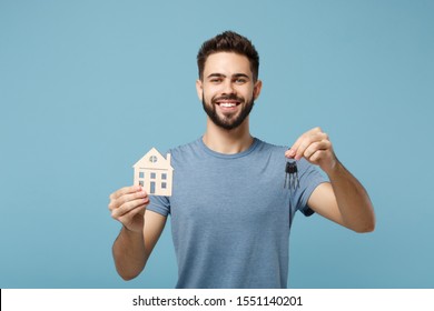 Young smiling man in casual clothes posing isolated on blue wall background, studio portrait. People sincere emotions lifestyle concept. Mock up copy space. Holding in hands house and bunch of keys