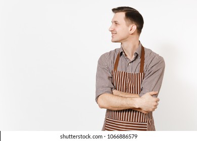 Young smiling man chef or waiter in striped brown apron, shirt holding hands crossed isolated on white background. Male housekeeper or houseworker looking aside. Domestic worker for advertisement - Shutterstock ID 1066886579