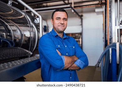 A young smiling man in a denim shirt at the cheese factory. An attractive worker near a milk and a butter making machine. An engineer for the maintenance of a cheese production line. Dairy equipment - Powered by Shutterstock