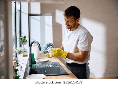 Young smiling man doing dishes in the kitchen. Copy space. - Powered by Shutterstock