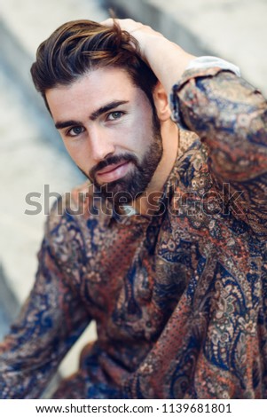 Guy with beard and modern hairstyle in urban background.