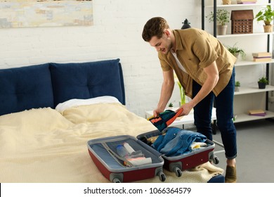 Young Smiling Man Packing Clothes Into Travel Bag