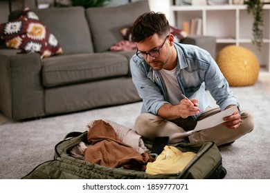 Young smiling man packing clothes into travel bag. Man preparing for the trip. - Powered by Shutterstock