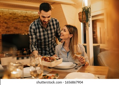 Young smiling man serving dinner to his girlfriend in dining room. 