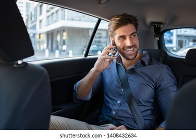 Young Smiling Man Talking Over Phone While Sitting In Taxi. Happy Business Man Sitting On Back Seat Of Car Using Mobile Phone To Communicate. Businessman Talking Over Cellphone While Commuting.