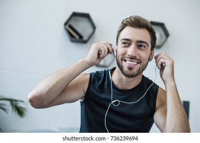 Young Smiling Man In Tanktop Putting On Earbuds And Looking Aside