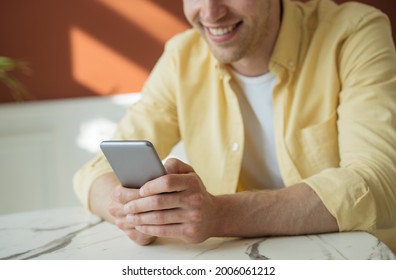 Young Smiling Man Using Mobile Phone Shopping Online, Making A Reservation Sitting In Cafe. Happy Freelancer Working From Home 