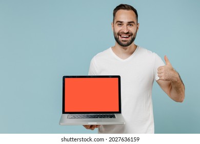 Young Smiling Man In White Blank Print Design T-shirt Hold Use Work On Laptop Pc Computer With Blank Screen Workspace Area Show Thumb Up Gesture Isolated On Plain Pastel Light Blue Background Studio