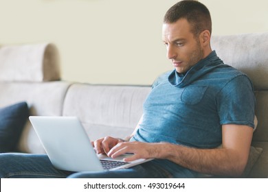 Young Smiling Man Working At Home And Using Laptop. Selective Focus And Small Depth Of Field.