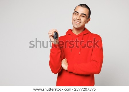 Young smiling middle eastern man he wears red hoody casual clothes hold in hand car fob keyless system look aside on area isolated on plain solid white background studio portrait. Lifestyle concept