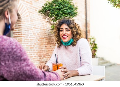 Young Smiling Millenial Friends Holding Hands In A Cocktail Bar Restaurant Outdoor Wearing Protective Face Mask During Happy Hour In An Outdoor Pub. Happy Couple Drinking After Coronavirus Reopening