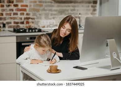 A young smiling mom is hugging a pretty daughter while she is drawing in the notebook at the workplace. A gorgeous mother is looking at her blonde child which is doing homework at home. - Powered by Shutterstock