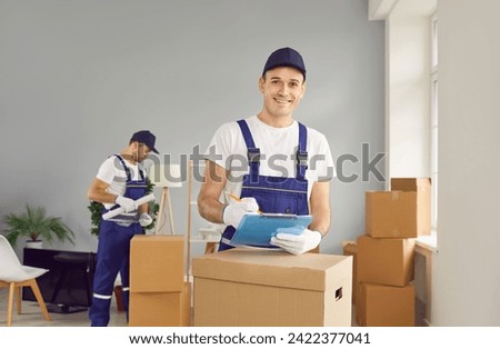 Young smiling mover man checking items list for moving, individual or company worker writing possessions, boxes, from one house to another, workman wearing uniform helping to change residence packing