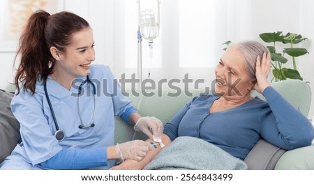 Young smiling nurse or doctor help sick senior elderly woman patient in receiving IV drip infusion and vitamin injection therapy sitting on sofa in medical clinic or at home. Health care concept