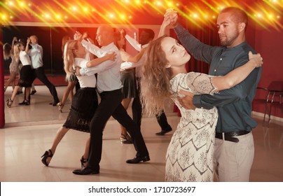 Young smiling people learning to dance waltz in dancing class