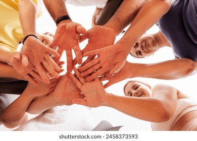 Young smiling people in sportswear putting hands together on light background. Women and men standing in circle and holding hands together. Bottom view. Unity and support concept. - Powered by Shutterstock