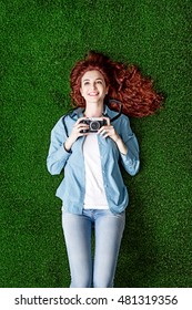 Young smiling photographer girl lying on the grass, she is relaxing and holding a digital camera