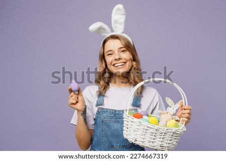 Young smiling positive fun cheerful woman wearing casual clothes bunny rabbit ears hold wicker basket show colorful egg isolated on plain pastel purple background studio portrait. Happy Easter concept